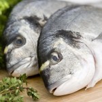 Two fresh sea bream on wooden board with herbs and lemon